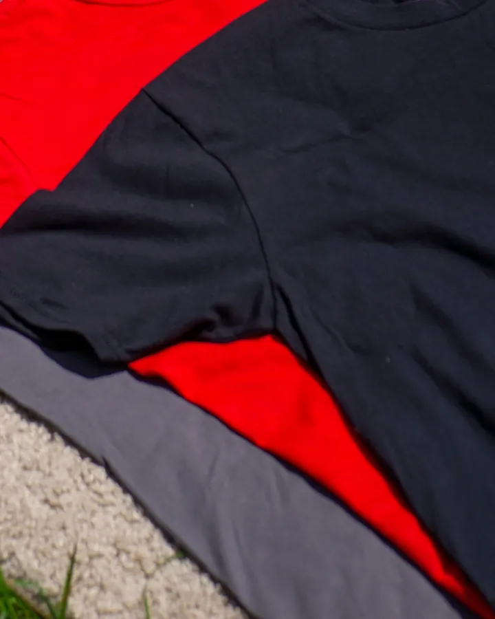 Plain black, red and grey t-shirts laid flat and overlapping on a cream rug in sunlight