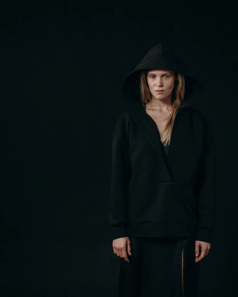 Woman in an oversized black hoodie with the hood up, against a black background