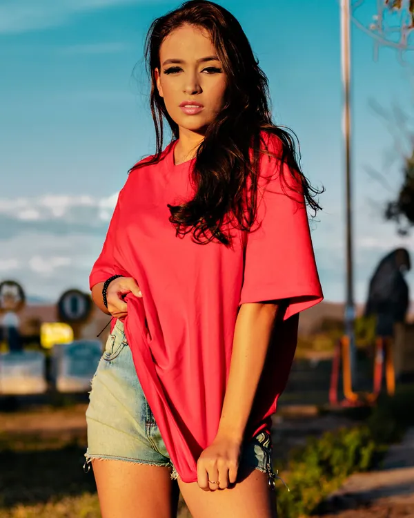 Woman in an oversized plain red t-shirt and denim shorts outdoors under a blue sky