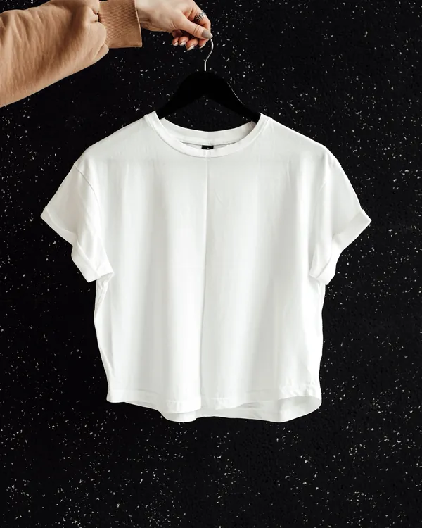 Plain white t-shirt on a black hanger, held up against a black speckled wall