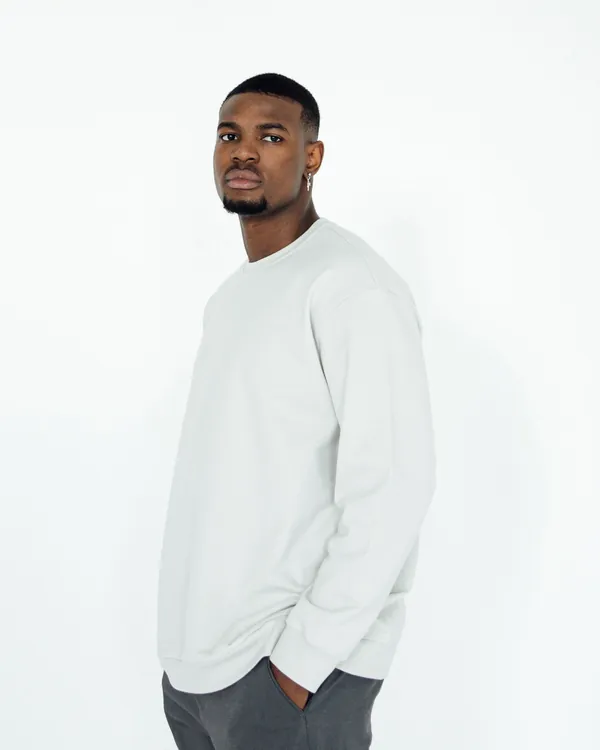 Man in a plain off-white crewneck sweatshirt and grey trousers against a white studio wall